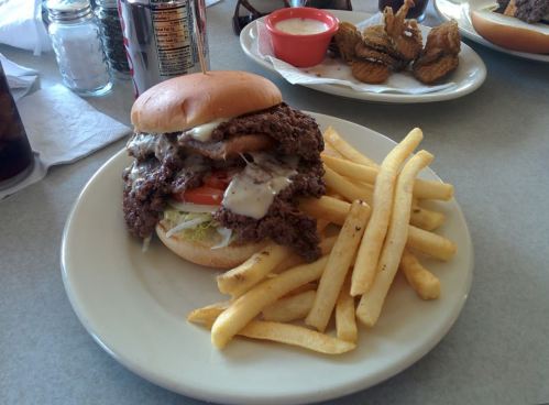A large burger with lettuce, tomato, and sauce, served with fries on a plate, alongside a small bowl of dipping sauce.