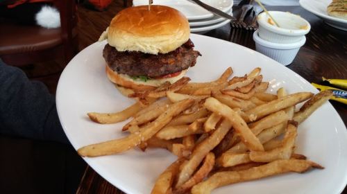 A juicy burger with lettuce and tomato on a bun, served with a side of golden French fries on a white plate.