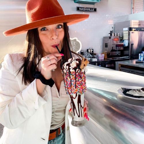 A woman in a wide-brimmed hat enjoys a colorful ice cream sundae topped with sprinkles and whipped cream.