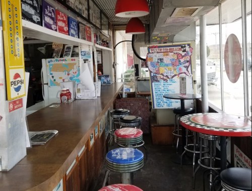 A retro diner interior with a wooden counter, colorful stools, and maps on the walls, creating a nostalgic atmosphere.