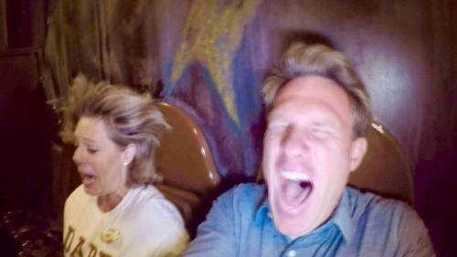 A man and woman scream in excitement on a roller coaster, their hair blown back by the speed.