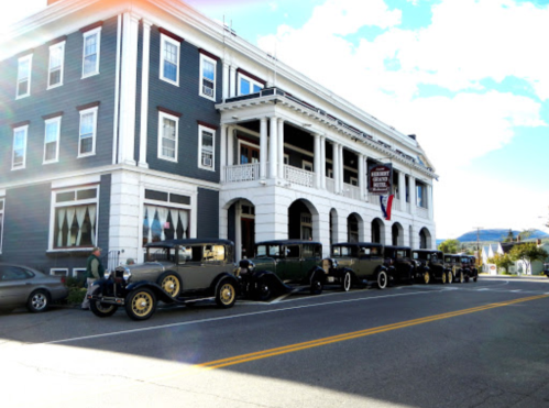 A row of vintage cars parked in front of a historic building on a sunny day.