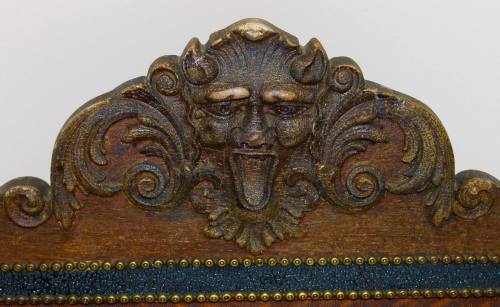 Carved wooden ornament featuring a grotesque face with horns and a protruding tongue, surrounded by ornate scrollwork.