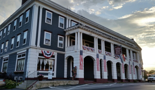 Historic hotel with patriotic decorations, featuring a large porch and columns, set against a cloudy sky.