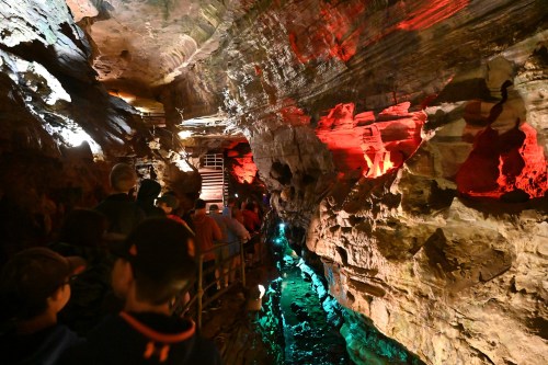 A group of people exploring a colorful cave with illuminated rock formations and a waterway.