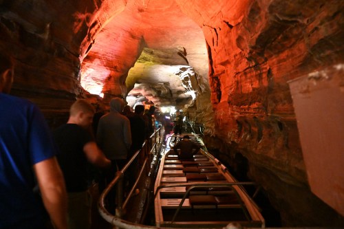 Visitors line up beside a boat in a colorful, illuminated cave with rocky walls and water below.