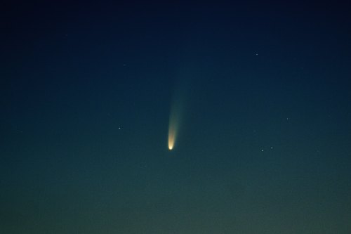 A bright comet with a long tail streaks across a dark night sky filled with stars.