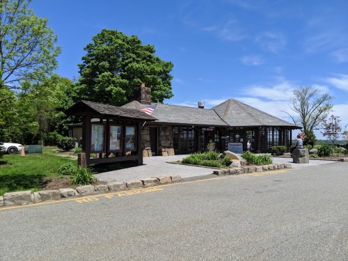 A stone and wood building with large windows, surrounded by greenery and a clear blue sky.
