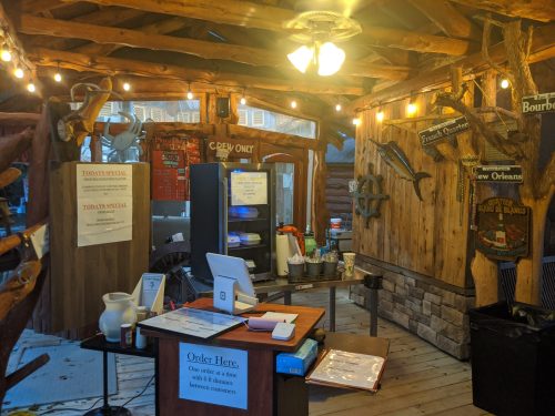 Cozy wooden restaurant interior with a counter, menu signs, and warm lighting. A special board is visible.