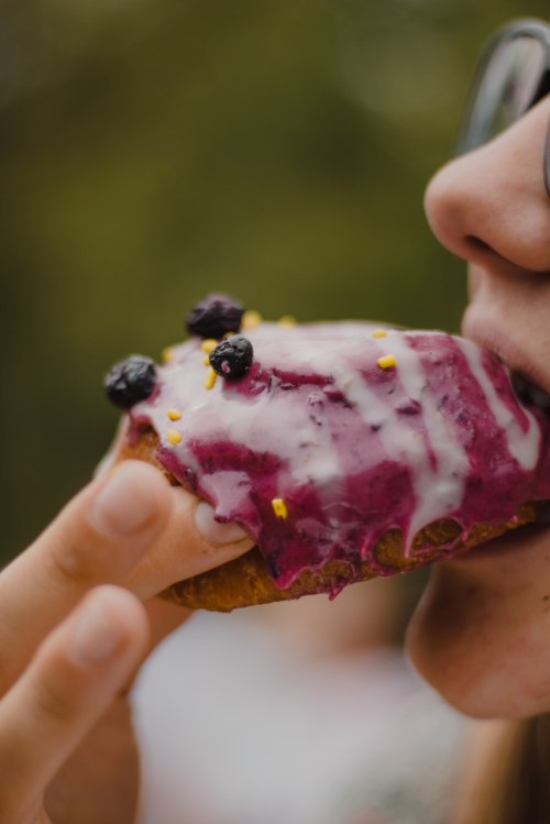 A close-up of a person about to bite into a colorful dessert topped with berries and icing.