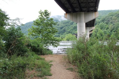 A riverbank scene with lush greenery and a bridge overhead, surrounded by rolling hills and misty clouds.