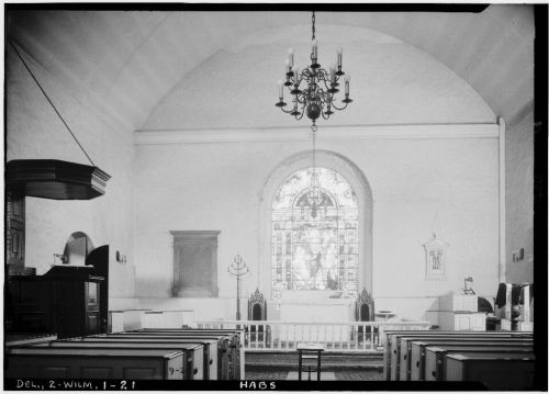 Interior of a church featuring a stained glass window, pews, and a chandelier, captured in black and white.