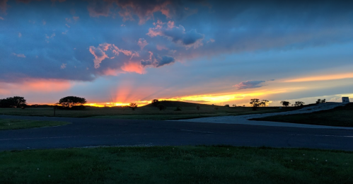 A vibrant sunset with colorful clouds and rays of light over a grassy landscape and winding road.