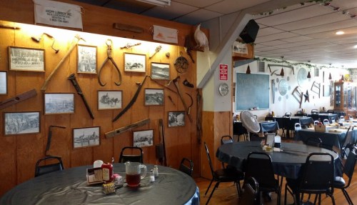 Interior of a rustic restaurant featuring wooden walls adorned with vintage tools and framed historical photos.