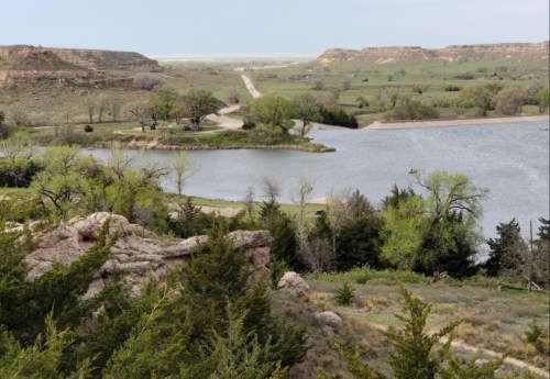 A scenic view of a winding river surrounded by green trees and rolling hills under a clear sky.