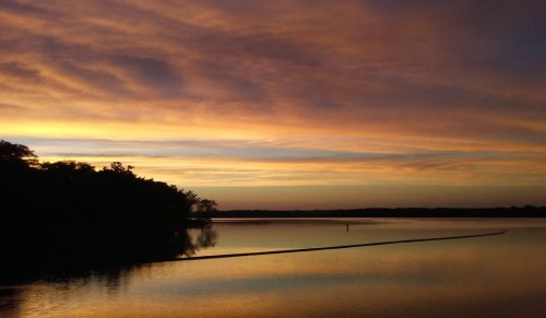 A serene sunset over a calm lake, with vibrant orange and purple hues reflecting on the water's surface.