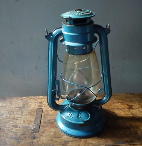 A vintage blue lantern with a glass globe, resting on a wooden surface against a plain background.