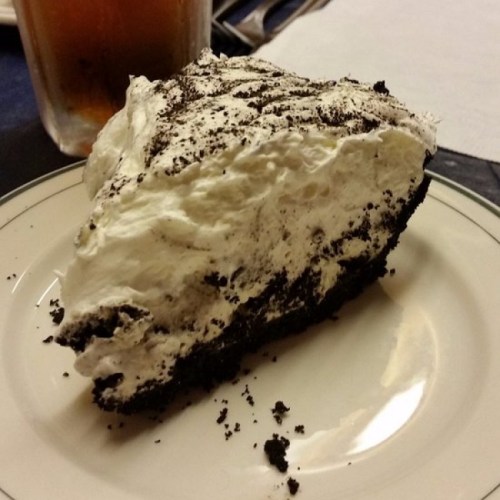 A slice of chocolate cream pie with a fluffy whipped topping on a white plate, crumbs scattered around.