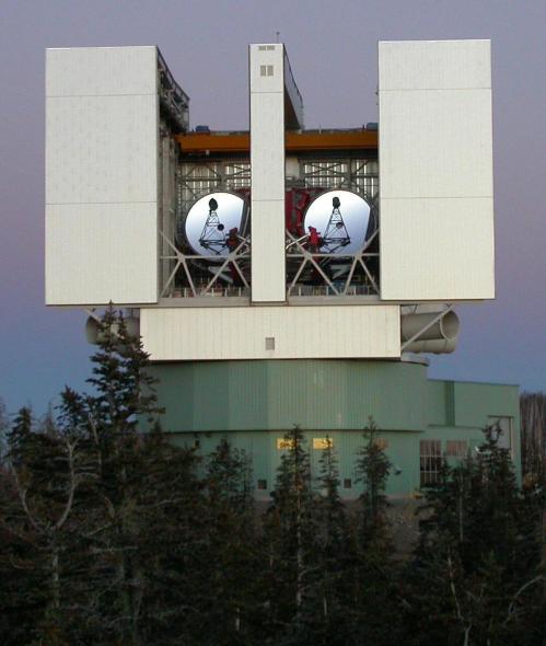 A large satellite dish facility surrounded by trees, featuring two prominent satellite dishes on a modern structure.