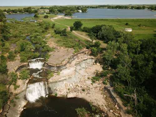 Aerial view of a waterfall cascading into a river, surrounded by lush greenery and a scenic landscape.