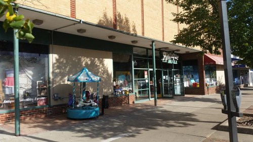 Exterior of an antique mall with a colorful carousel display outside, surrounded by trees and sidewalk.