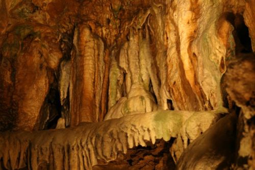 Stalactites and stalagmites in a cave, showcasing intricate textures and earthy colors illuminated by soft lighting.