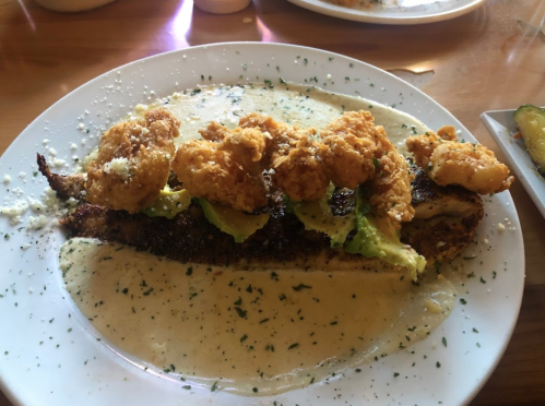 A plate of blackened fish topped with fried shrimp, served with a creamy sauce and garnished with herbs.