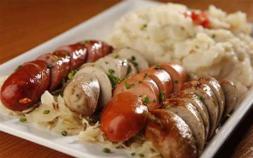A platter of assorted sausages served with sauerkraut and mashed potatoes, garnished with chives.