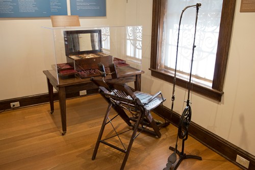 A vintage dental chair and equipment displayed in a museum setting, with natural light coming through a window.