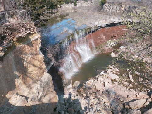 A waterfall cascading over rocky cliffs into a serene pool, surrounded by trees and rugged terrain.