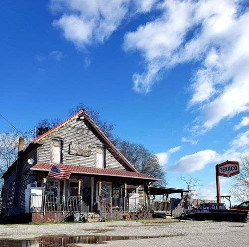 A vintage wooden building with an American flag, a Texaco sign, and a clear blue sky in the background.