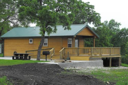 A wooden cabin with a green metal roof, featuring a deck and surrounded by trees and grass.