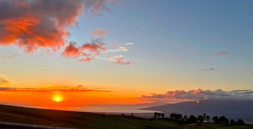 A vibrant sunset over the ocean, with clouds and distant mountains silhouetted against the colorful sky.