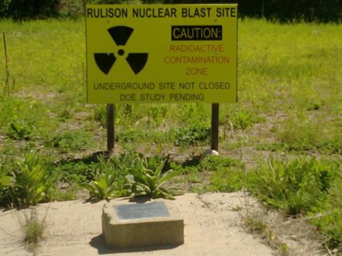 Sign at the Rulison Nuclear Blast Site warns of radioactive contamination and pending studies. Green grass surrounds the area.