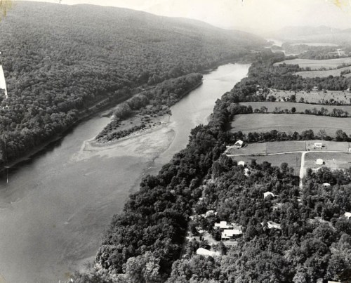 Aerial view of a river winding through lush green hills and farmland, with scattered houses along the banks.