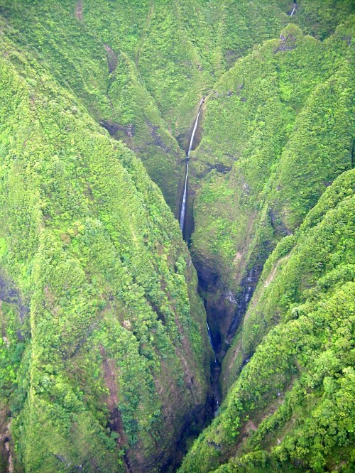 Aerial view of lush green mountains with a waterfall cascading down a steep valley.