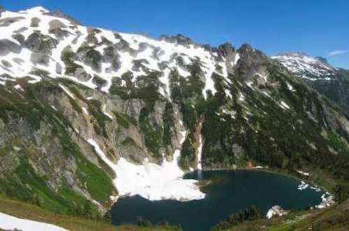 A scenic mountain landscape featuring snow-capped peaks and a serene lake surrounded by lush greenery.