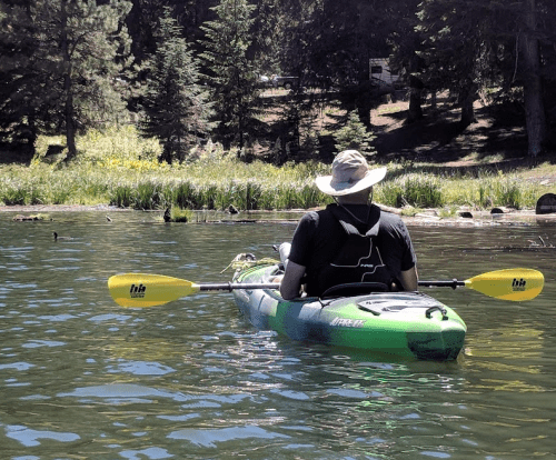 A person in a kayak paddles on a calm lake surrounded by trees and greenery.