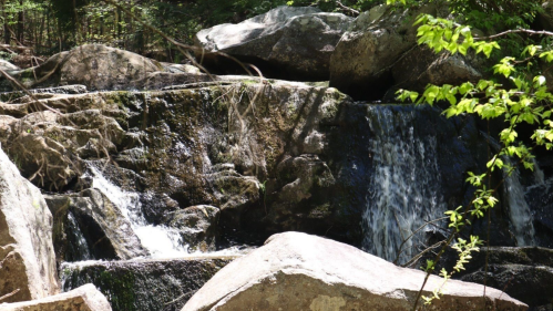 A serene waterfall cascading over rocky terrain, surrounded by lush greenery and sunlight filtering through the trees.