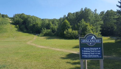A green landscape with a sign for Avalanche, featuring hiking, biking trails, and a disc golf course.
