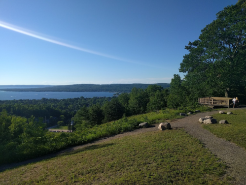 A scenic view of a lake surrounded by green hills, with a path and a wooden overlook in the foreground.