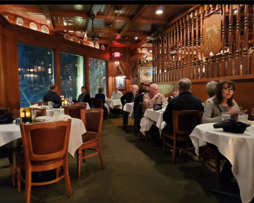 A cozy restaurant interior with wooden decor, tables set for dining, and patrons enjoying their meals in a warm atmosphere.