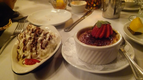 A plate with a creamy dessert topped with a strawberry and a side of whipped cream drizzled with chocolate sauce.