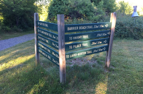 Wooden signpost with directional arrows for various trails, including Barrier Beach, Knight, Pilger, and Laird-Norton Trails.