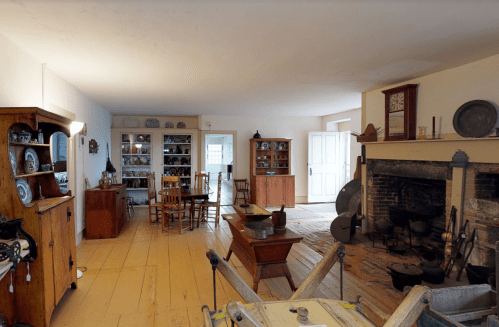 A cozy, historic room with wooden furniture, shelves of dishes, and a fireplace, showcasing a vintage interior.