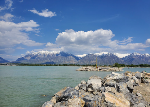 A scenic view of a lake with rocky shores, mountains in the background, and a partly cloudy blue sky.