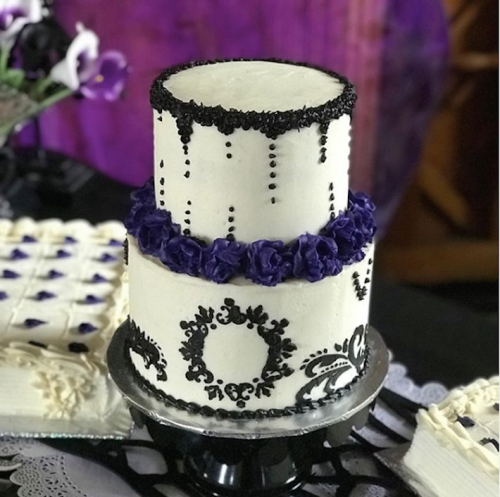 A two-tiered cake decorated with black and purple icing, featuring floral accents and elegant patterns.
