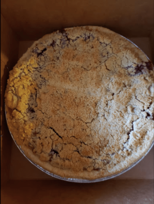 A round pie with a golden, crumbly topping, partially visible in a cardboard box.