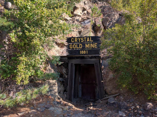 Entrance to the Crystal Gold Mine, established in 1881, surrounded by trees and rocky terrain.