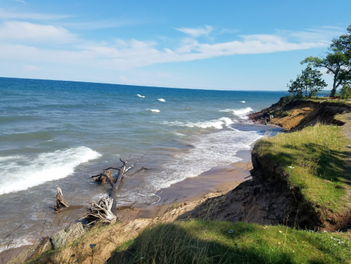 A scenic view of a shoreline with waves, sandy beach, and eroded cliffs under a clear blue sky.